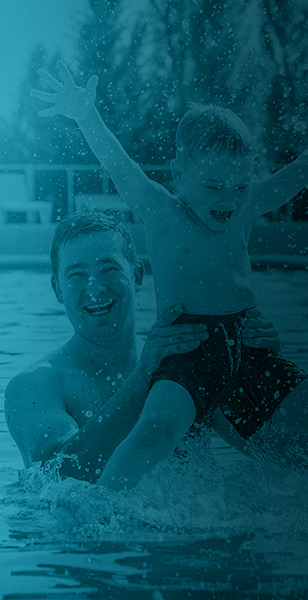 Father and son smiling and playing in a pool.