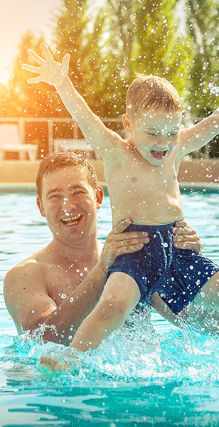 Father and son smiling and playing in a pool.