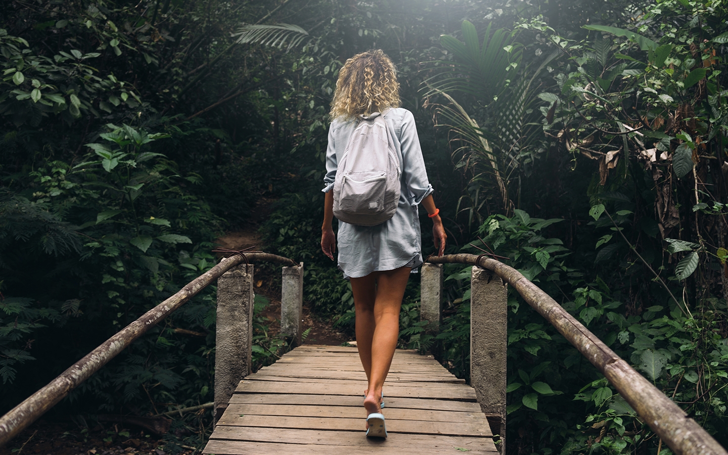 Blonde woman walking along a forest bridge.