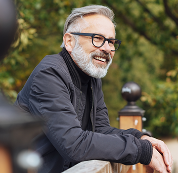 Older man with glasses looking out over a bridge.