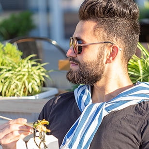 Young man eating food in an outside seating area.