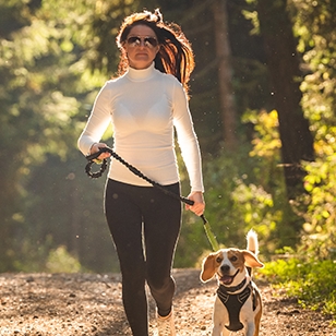 Woman in sunglasses running along a forest trail with her dog.