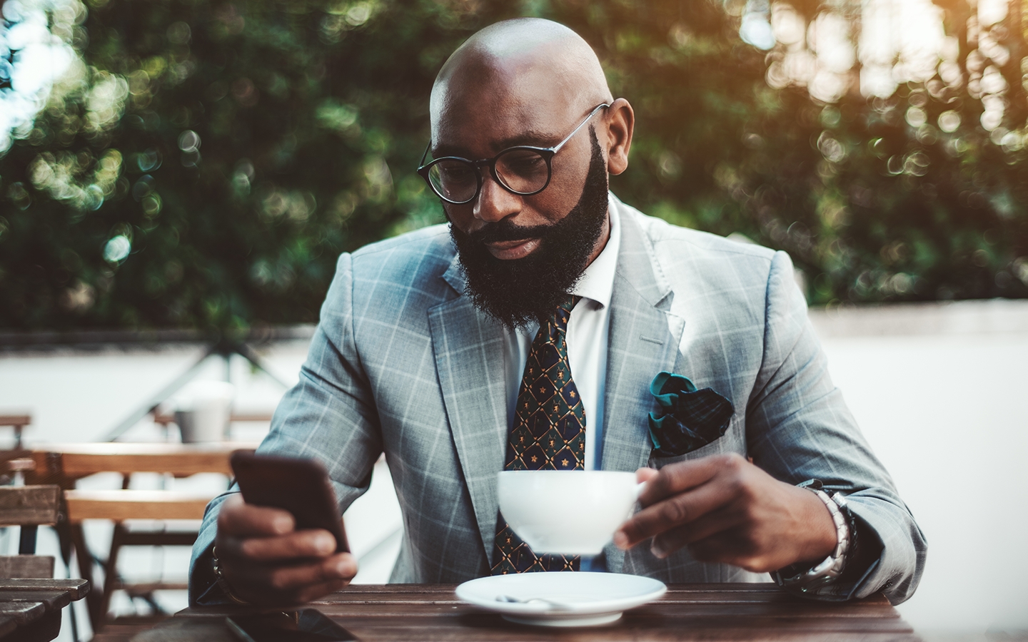African American man in suit looking at phone over coffee.