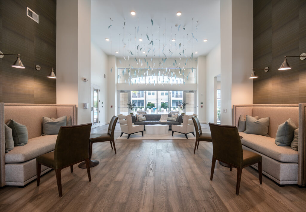 A modern lounge with high ceilings, beige seating, brown chairs, and hanging glass art. Large windows let in natural light, and neutral tones create an inviting, elegant atmosphere.